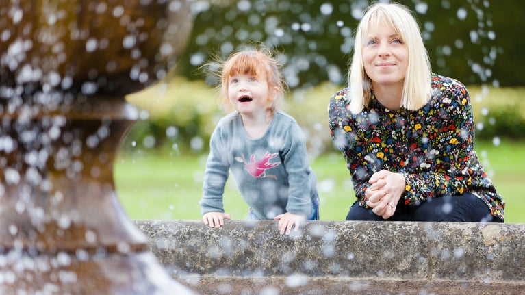 A lady smiling and a young girl with a face full of wonder watching water fall from a fountain at Powis Castle, Powys, Wales